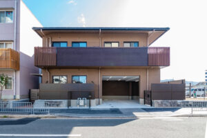 現代的な介護施設の建物外観。茶色いタイルと木調パネルの外壁に大きな窓が特徴。